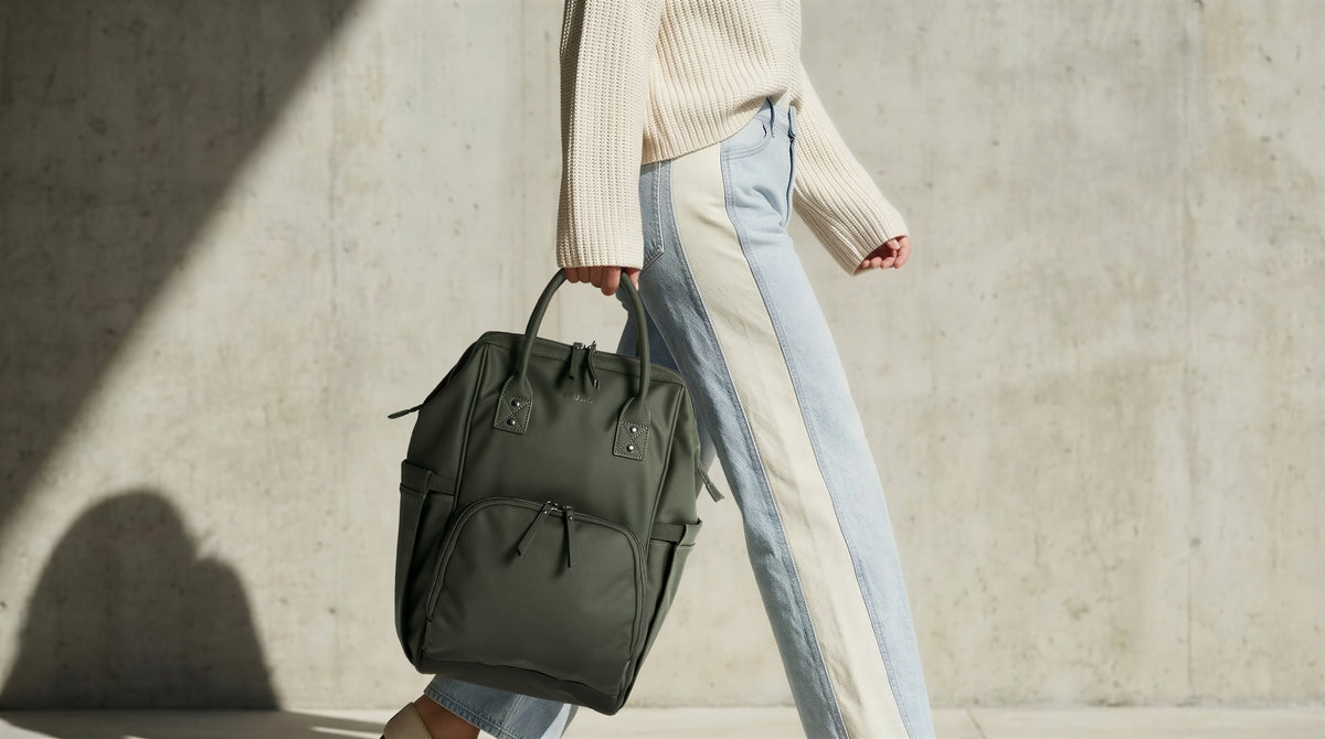 Woman carrying the olive green ALUXO Active X baby bag by its top handle against a concrete wall
