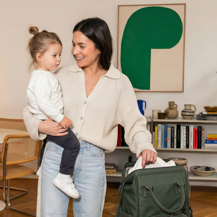Mum holding her toddler while packing the olive green ALUXO Active X baby bag at home