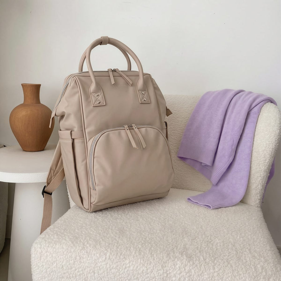 Stone ALUXO Active X baby bag on a white boucle chair beside a lilac throw
